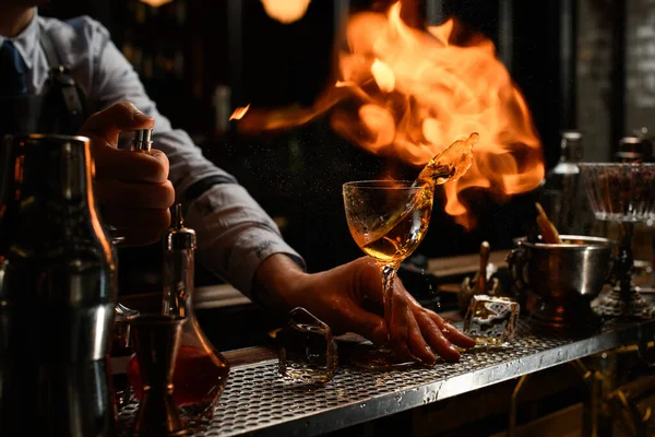 bartender holds by hand glass with splashed alcohol drink.