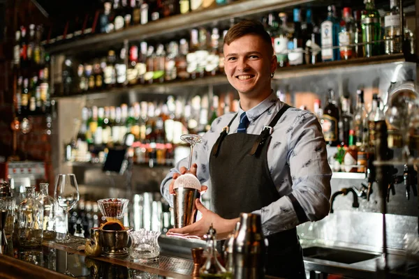 Ung leende bartender i svart förkläde förbereder sig för att göra cocktail. — Stockfoto
