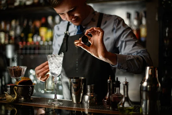Young smiling bartender professionally pour drink to shaker using beaker. — Stock Photo, Image