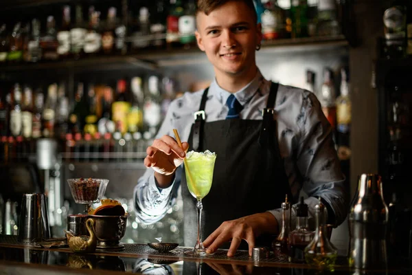 Ung leende bartender dekorerar cocktail med is i glas med två pinnar. — Stockfoto