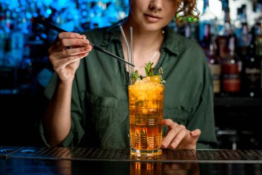 Cımbız kullanan kadın nazikçe cam çubuklarla kokteyl süslüyor.