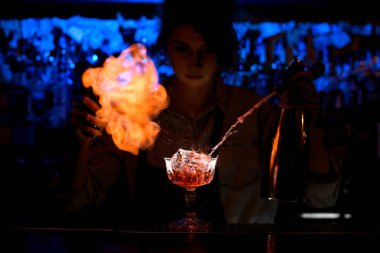 Profesyonel kadın barmen tezgahta cam üzerinde ustaca ateş yakıyor..