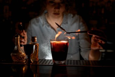 Profesyonel kadın barmen kırmızı kokteyl süsler, üzerine şeker serper ve ateş yakar..