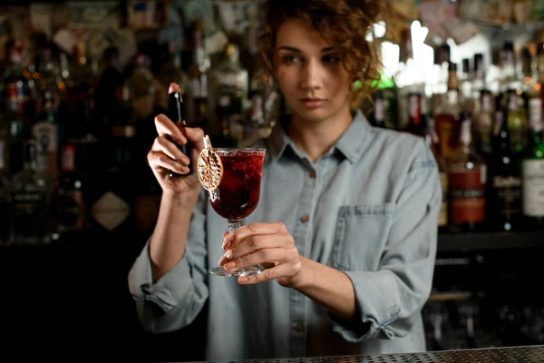 Молодая женщина бармен держать стакан напитка в руке — стоковое фото