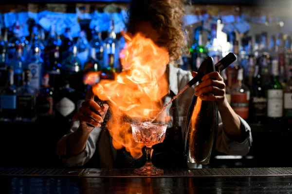 Женщина-бармен распыляет из металлического сифона в стекло и разжигает над ним огромный огонь. . — стоковое фото