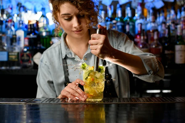 Молодая бармен тщательно готовит коктейль с ломтиками цитрусовых — стоковое фото
