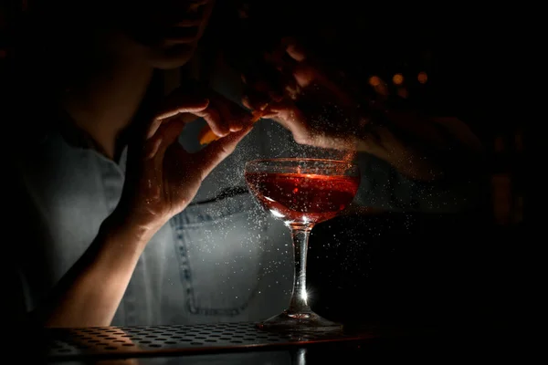 Vrouw barman zorgvuldig besprenkelt citrussap op wijnglas met cocktail aan de bar — Stockfoto