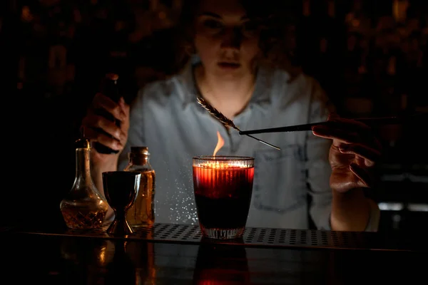 Mujer barman decora cóctel rojo, espolvorea sobre él y hace fuego . —  Fotos de Stock