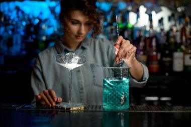 Kadın barmen kaşıkla büyük bardağa kokteyl karıştırıyor..