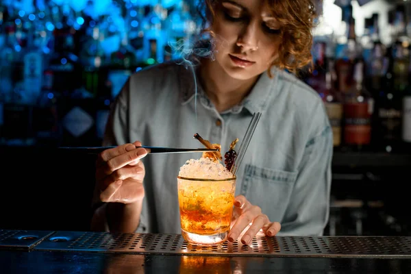 Lady bartender accurate decorates bright cocktail like negroni using tweezers.