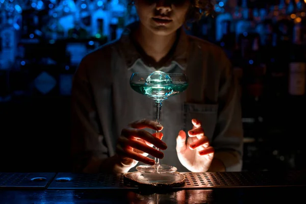 lady at bar holds very beautiful glass of blue cocktail.