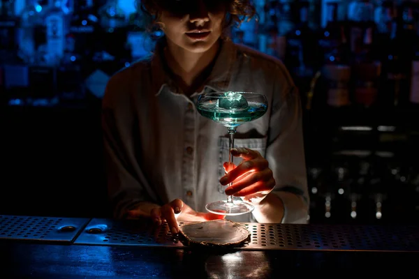 Mulher barman cuidadosamente mantém belo copo de coquetel azul . — Fotografia de Stock
