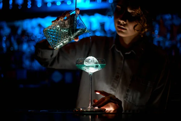 Woman at bar carefully pours cocktail into glass.