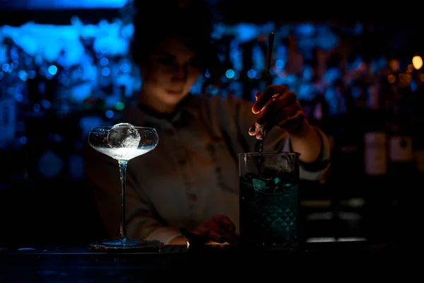 Mujer en el bar oscuro mezcla cóctel en vidrio grande con cuchara . —  Fotos de Stock