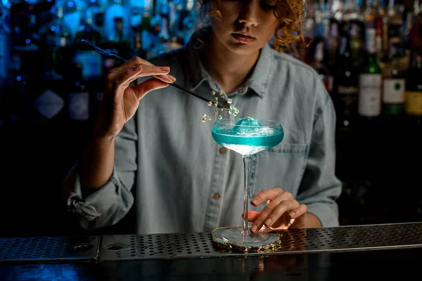 Леди бармен мастерски украшает стекло голубым напитком цветочная ветвь и посмотрите на него . — стоковое фото