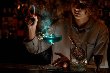 Kadın barmen, bardağa mavi kokteyl serpiştiriyor.