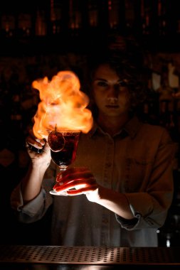 Barda elinde şarap kadehi olan bir kadın ustaca ateş yakıyor..