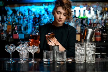 Barmen kadın içki bardağını jigger kullanarak dolduruyor.