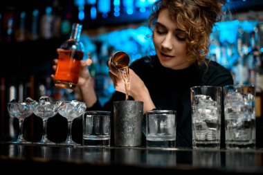 Bardaki genç ve güzel kadın, kahverengi alkoliği bardağa dolduruyor..