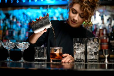 Güzel kadın barmen kokteyl hazırlıyor ve bardağa döküyor..