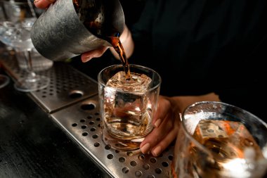 Yakın plan barmen negroni kokteylini tezgahın üzerine bardağa döküyor..