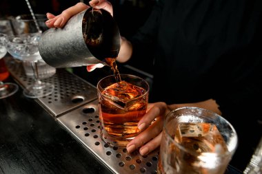 Yakın plan. Barmenlerin elleri bardaki bardaklara kokteyl doldurur..