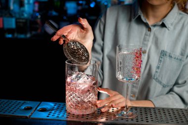 Barmen eli, büyük bardağın üzerinde pembe içecekle süzgeç tutuyor.