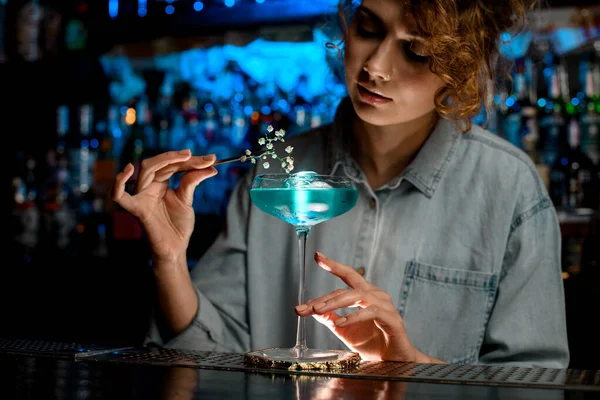 Lady bartender decora vidro com ramo de flor de bebida azul e olhar para ele . — Fotografia de Stock