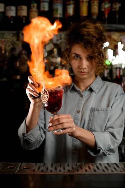 Профессиональная бармен держит бокал вина с коктейлем и пламя над ним . — стоковое фото