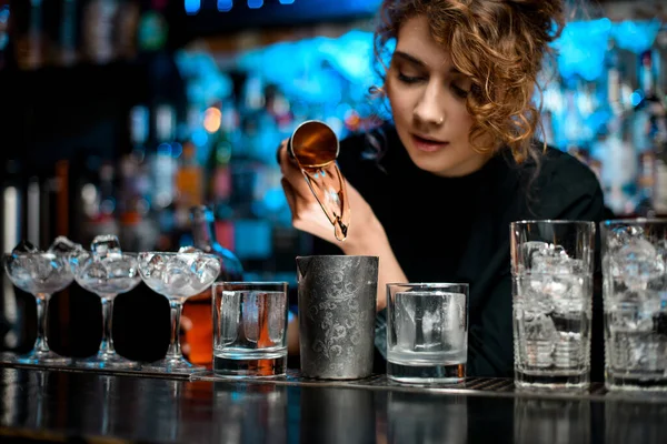 Fiatal csinos nő a bárban önti italt fém üveg segítségével acél jigger. — Stock Fotó