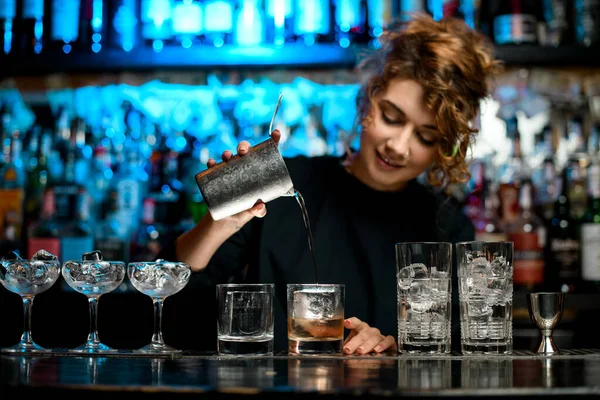 Lady barman carefully pours finished cocktail into glass.