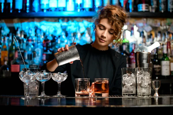 Young woman barman preparing cocktail and pouring it into glass. — Stock Photo, Image