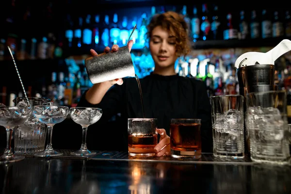 Young lady at bar pours alcoholic cocktail into glass.