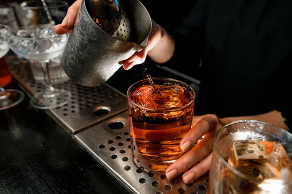 Yakın plan. Barmenlerin elleri bardaki bardaklara negroni kokteyli döker..