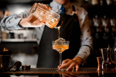 Barmen kadehten bardağa soğuk kokteyl doldurur..