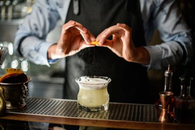 Siyah önlüklü barmen bardaklara narenciye suyu serpiyor..