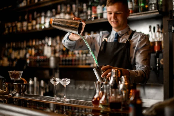 Mladý usměvavý barman nalévá koktejl v ocelovém třepačce. — Stock fotografie