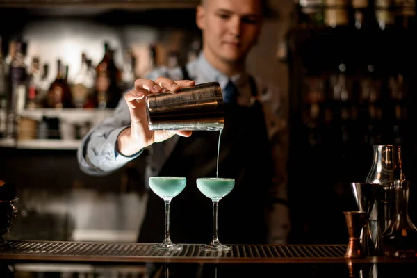 Joven barman profesionalmente vierte cóctel preparado de coctelera en vidrio . — Foto de Stock