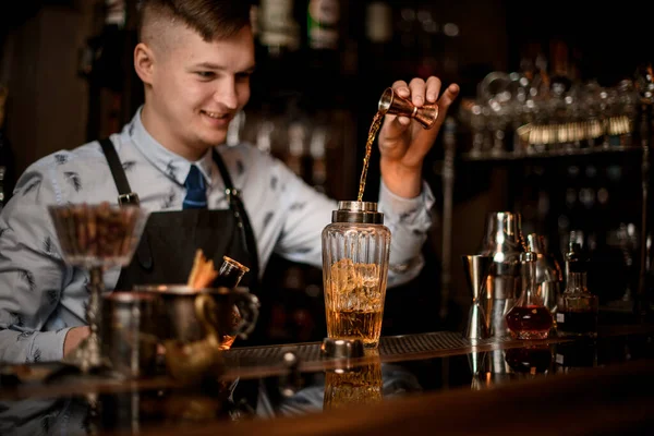 Jeune barman souriant verse soigneusement boisson à shaker vitreux à l'aide de bécher . — Photo