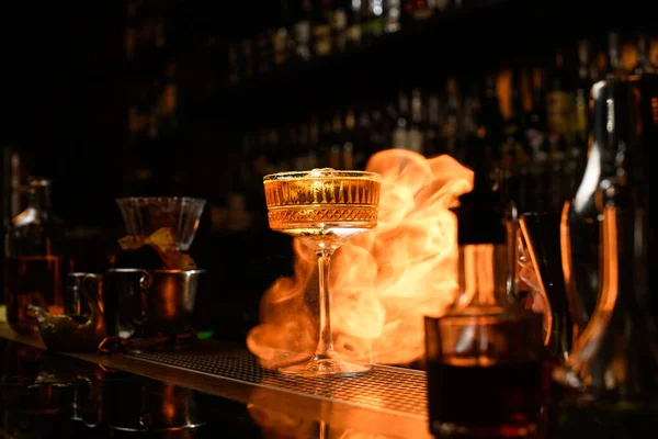 Glass of alcoholic drink and ice stands on bar counter. Fire flame behind it. — Stock Photo, Image