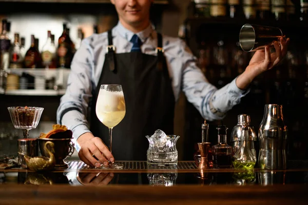 Ung leende bartender i svart förkläde håller glas med färdiga cocktail — Stockfoto