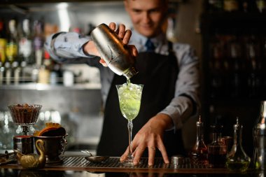 Barmen içkisini bardaktan bardağa doldurur.