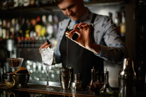 Joven barman profesional y cuidadosamente vierte bebida verde a agitador de acero usando vaso de precipitados . — Foto de Stock