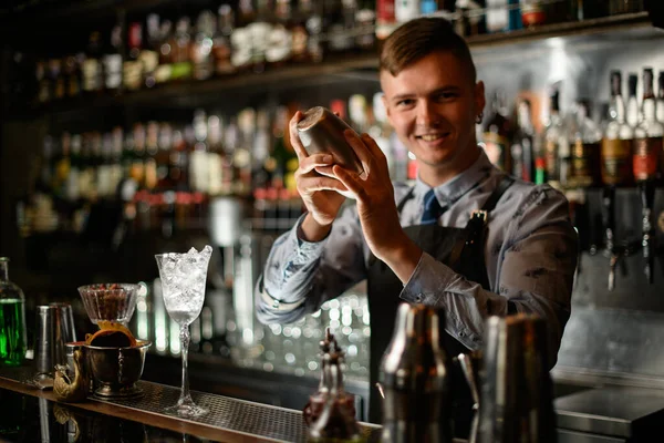 Młoda uśmiechnięta barmanka stojąca za barem z wytrząsarką stalową. — Zdjęcie stockowe