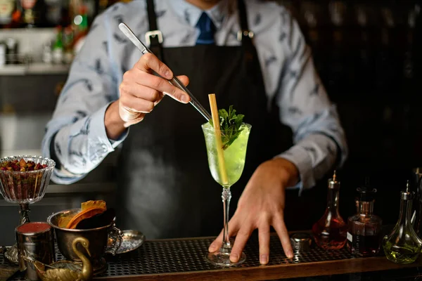 Barman décore cocktail prêt à l'emploi avec deux bâtons de feuilles de menthe à l'aide de pince à épiler — Photo