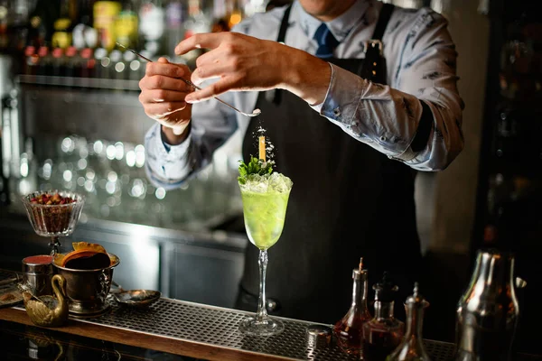 Barman v černé zástěře jemně zdobí koktejlové sklo práškem — Stock fotografie