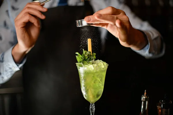 Barman decorates by powder ready-made cocktail with two sticks and mint leaves — Stock Photo, Image