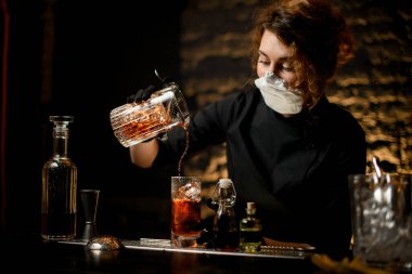 Bardaki genç bir kadın bardağa soğuk kokteyl dolduruyor..