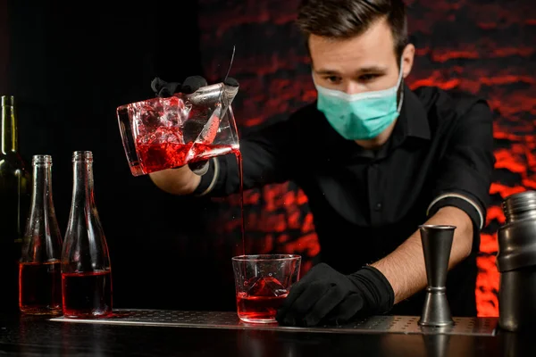 Barman con máscara vierte magistralmente cóctel frío en el vaso . — Foto de Stock