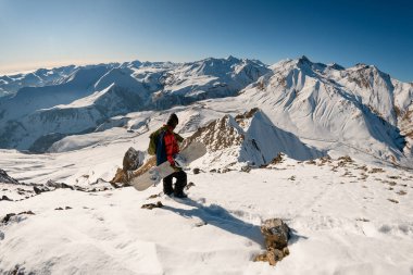 Snowboardcu karlı dağda durur ve aşağıya bakar.